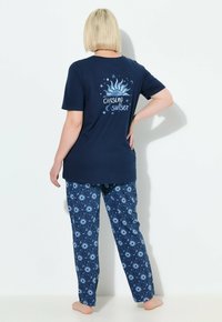 Marine t-shirt met een grafisch ontwerp van een zon en de tekst "Chasing Sunset," gecombineerd met een gestreepte pyjamabroek met blauwe en witte sterachtige ontwerpen.