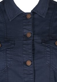 Chaqueta de mezclilla azul marina con cuello puntiagudo, botones de bronce y detalles cosidos, con dos bolsillos en el pecho y un bolsillo lateral.