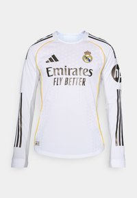 Hvid langærmet fodboldtrøje med sorte striber, Adidas-logo og Real Madrid's klubmærke. "Emirates Fly Better" præsenteres tydeligt.