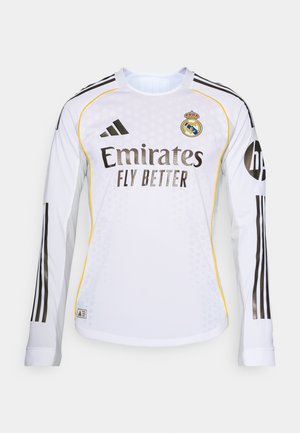 Maglia da calcio a maniche lunghe bianca con strisce nere, logo Adidas e il simbolo del Real Madrid. La scritta "Emirates Fly Better" è ben in evidenza.