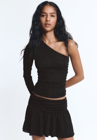 Fekete, egyvállas felső redős textúrával, az egyik oldalon hosszú ujjú. Fekete, bővülő mini szoknyával párosítva, mindkettő finom csillogással.