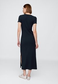 Sort, tætsiddende kjole med korte ærmer og lige snit med slidser i siderne, lavet af blødt stof, kombineret med lyse sneakers.