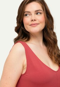 Tanktop mit weitem Rundhalsausschnitt aus weichem, rotem Stoff. Verfügt über breite Träger und ein figurbetontes Design. Glatte Textur mit einem schlichten, eleganten Profil.