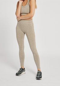 Beżowe legginsy sportowe i dopasowany crop top. Lekki, miękki materiał o heatherowanej teksturze. Detale z logo na klatce piersiowej i w talii.