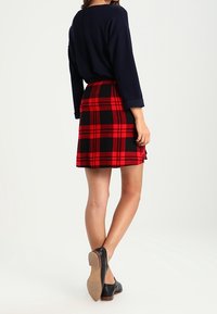 Punainen ja musta ruudullinen minisatiinihame, jossa on istuva vyötärö ja levenevä helma, yhdistettynä laivastonsiniseen ylisuurteen paitaan ja mustiin tasapohjaisiin kenkiin.