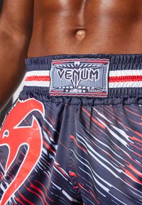 Marineblaues Shorts mit einem rot-weißen abstrakten Muster, ausgestattet mit einem gewebten VENUM-Logo-Patch am elastischen Bund und gestreiften Akzenten.