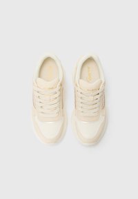 Scarpe sportive beige con una tomaia testurizzata color crema, dettagli in mesh e punta arrotondata. Presentano lacci piatti e una suola imbottita.
