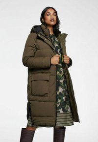 Olivgrön vadderad jacka med huva, dragkedja framtill och stora sidofickor. Innerlagret har en kamouflagemönstrad design med ett mönstrat fåll.