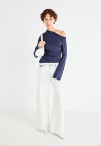 Top bleumarin cu umeri descoperiți, cu textură plisată, asortat cu blugi albi cu talie înaltă și pantalonii largi, completat cu o geantă mică albă.