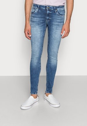 Vaqueros de corte ajustado en denim azul claro, con un acabado desgastado, diseño de cinco bolsillos y cierre de cremallera. Combinados con zapatillas blancas de tipo slip-on.