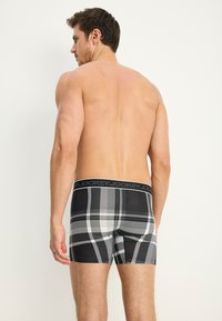 Svarta boxerkalsonger med en rutigt mönster i grått och vitt. Midjebandet visar varumärket "Jockey." Tillverkade av ett flexibelt material.