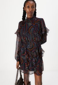 Vestido escuro com padrão de paisley, apresentando mangas em babados e um decote alto. Feito de tecido transparente com detalhes de cor intrincados.