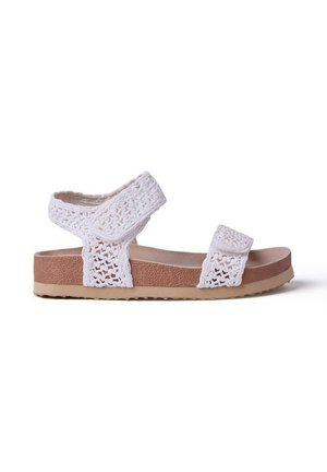 Sandalias de tela de crochet blanco con dos tiras ajustables de velcro y una suela marrón texturizada sobre un fondo blanco.