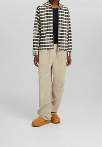 Zwart-wit geruite jas met rits over een zwart shirt, gecombineerd met beige corduroy broek en tan instapschoenen. Gestructureerde, casual outfit.