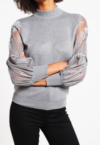 Gray knitted sweater with a mock neck, featuring sheer, striped puff sleeves adorned with floral embroidery. Fitted design, ribbed cuffs.