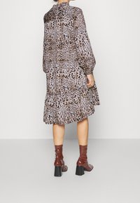 Šaty s leopardím potiskem vyrobené z průsvitné látky, s volánkovým lemem, dlouhými rukávy a vysokým výstřihem, v kombinaci s lesklými vínovými kotníkovými botami.