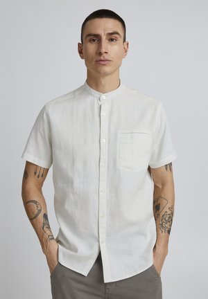 Short-sleeve, collared shirt in white linen, featuring a pocket on the left chest and a button-down front. Smooth, lightweight texture.