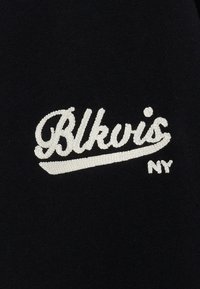 Czarna tkanina z białym haftowanym napisem "Blkvis" oraz "NY" poniżej, z użyciem zabawnej, kursywnej czcionki i gładkiej tekstury.