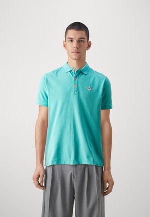 Camisa polo turquesa de algodón, con un cuello, una tapeta de tres botones con botones naranjas y un pequeño parche de logo en el pecho.