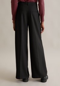 Zwarte wijde pantalon gemaakt van soepel stof, met een achterzak en een hoge taille. Te combineren met chunky zwarte schoenen.