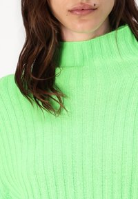 Pulover turtleneck ribbed de culoare verde aprins, cu o textură moale. Materialul prezintă dungi verticale și un design cu guler înalt.