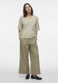 Beżowa koszulka w paski z dekoltem w serek oraz ciemnozielone spodnie w szerokie nogawki w kolorze khaki, z mankietami i czarnymi loafersami.