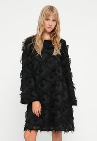 Μαύρο φόρεμα με άνετη εφαρμογή, που διαθέτει υφασμάτινη υφή με επίπεδες φούντες, μακριά μανίκια και στρογγυλή λαιμόκοψη.