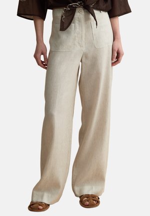 Pantaloni beige a gamba larga con righe verticali, tasche applicate frontali, chiusura con bottoni e zip, indossati con top marrone annodato e sandali marroni.