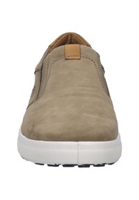 Beżowe zamszowe buty wsuwane o teksturowanej powierzchni, biała gumowa podeszwa i mały brązowy akcent na górze. Wąski, zaokrąglony kształt nosa.