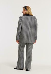 Zwart-wit houndstooth pak met een lange, op maat gemaakte blazer en flared broeken, met een gladde textuur en een gestructureerd ontwerp.