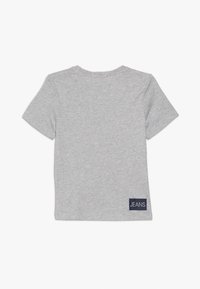 Grijze katoenen t-shirt met korte mouwen, ronde hals en een navy blauwe label met "JEANS" aan de onderkant aan de linkerkant. Zachte structuur, casual ontwerp.