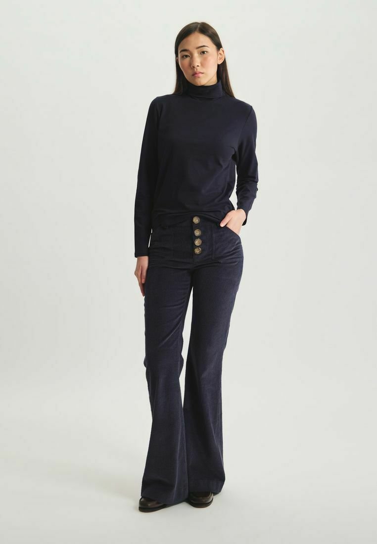 Un haut col roulé marine associé à un pantalon en velours côtelé évasé taille haute de couleur marine, doté de cinq boutons ronds à l'avant. Texture lisse.