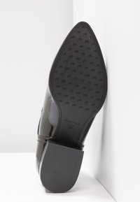 Escarpin en cuir verni noir avec une semelle en caoutchouc texturé. Présente une forme de bout triangulaire et un logo de marque embossé. Taille 37 marquée à l'intérieur.