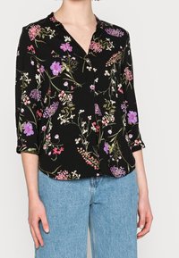 Blusa nera con stampa floreale vivace in rosa, viola e verde. Presenta un colletto e maniche a tre quarti.