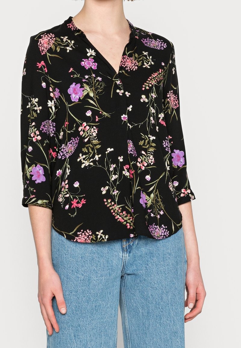 Blusa nera con stampa floreale vivace in rosa, viola e verde. Presenta un colletto e maniche a tre quarti.