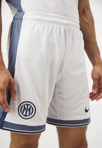 Witte en marineblauwe sportshorts met een elastische tailleband, voorzien van een cirkelvormig logo en contrasterende zijpanelen, een gladde textuur en afgewerkte accenten.