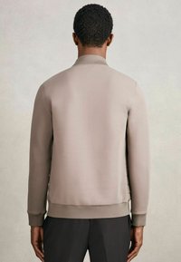 Lyst beige bomberjakke med en glat overflade, ribbet krave og manchetter, samt en afslappet pasform. Minimalistisk design uden synligt hardware.