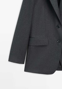 Mørkegrå blazer med struktureret stof, to knapper, en enkelt brystlomme og en let struktureret pasform.