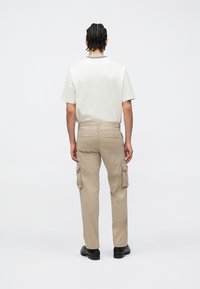 Μπεζ παντελόνι cargo με πολλαπλές πλαϊνές τσέπες, συνδυασμένο με μια κρεμ κοντομάνικη μπλούζα. Το ύφασμα φαίνεται λείο και η εφαρμογή είναι χαλαρή.