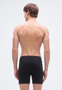 Juodi bokseriniai šortai iš lygios medžiagos, aptempto dizaino, su vidutinio aukščio juosmeniu, be matomų raštų ar akcentų. Vaizdas iš nugaros.