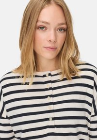 Gestreepte sweater in crème en marineblauw. Heeft een ronde halslijn, een knoopsluiting met parelknopen en een lichte gebreide textuur.