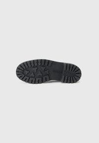 Semelle de chaussure noire en caoutchouc avec un motif de profil présentant des formes circulaires et triangulaires. "Mare O'Polo" embossé sur le côté.