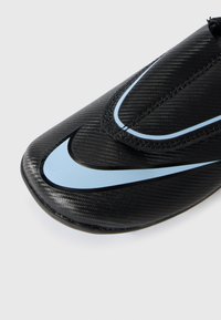 Gros plan sur l'orteil d'une chaussure de sport noire avec une surface texturée et le logo swoosh Nike bleu clair au-dessus.