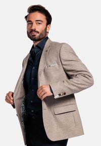 Beige wool blazer with a tailored fit, two front pockets, and floral-patterned lining. Paired with a dark blue shirt beneath.