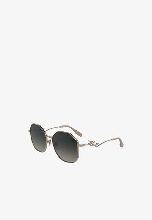 Óculos de sol octogonais com lentes escuras em degrade. Armação metálica em bege claro com detalhe assinado na haste, design leve e elegante.