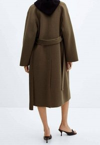 Manteau long en laine marron avec capuche noire, ceinturé à la taille, doté de manches larges et d'une coupe mi-longue. Texture lisse, détails minimaux.