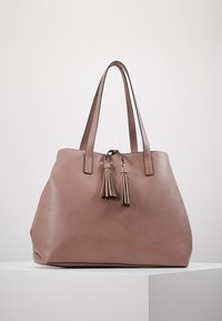 Sac cabas en cuir rose avec deux longs pampilles assorties, poignées robustes et design spacieux. Texture lisse et accents minimalistes.