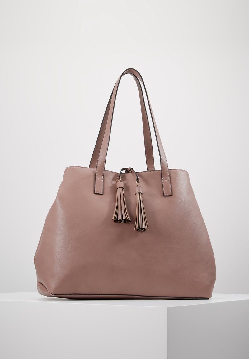 Sac cabas en cuir rose avec deux longs pampilles assorties, poignées robustes et design spacieux. Texture lisse et accents minimalistes.