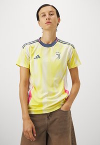 Gul och vit idrottströja med prickig textur, korta ärmar, blå krage och rosa sidovinklar. Har Juventus-logotyp och Adidas-ränder.