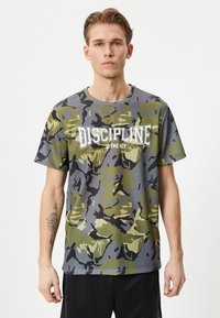 Camiseta de patrón de camuflaje en gris y verde, con un diseño de malla texturizada y el texto "LA DISCIPLINA ES LA CLAVE" en letras blancas.